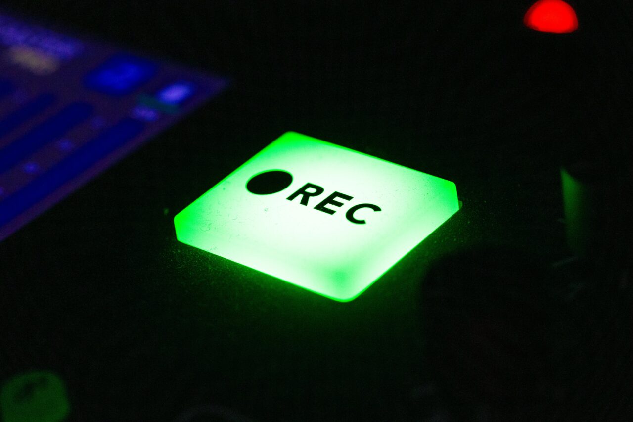 pexels-photo-24486666-24486666 Close-up of a green illuminated recording button on electronic device in low light.